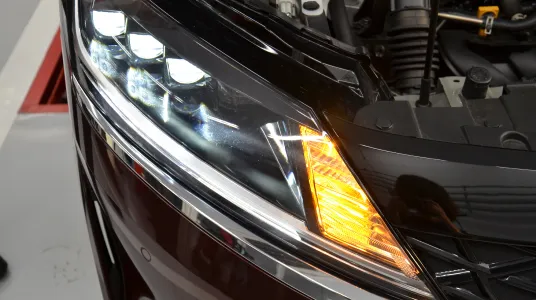 LED搭載のモダンな車のヘッドライト部分のクローズアップ。白色LEDのデイライトと黄色のウインカーが点灯している状態。光の反射が鮮明に写っている